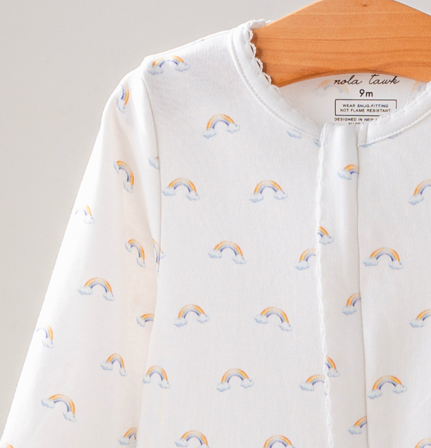 Baby outfit with rainbow patterns on a hanger against a neutral background