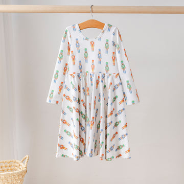 Organic cotton long-sleeve girls’ twirl dress with festive nutcracker print in red, green, and blue. Eco-friendly kids holiday clothing.