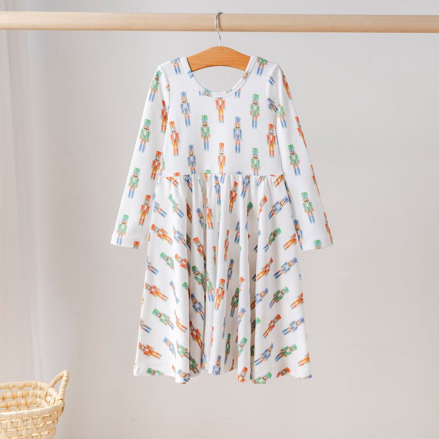 Organic cotton long-sleeve girls’ twirl dress with festive nutcracker print in red, green, and blue. Eco-friendly kids holiday clothing.